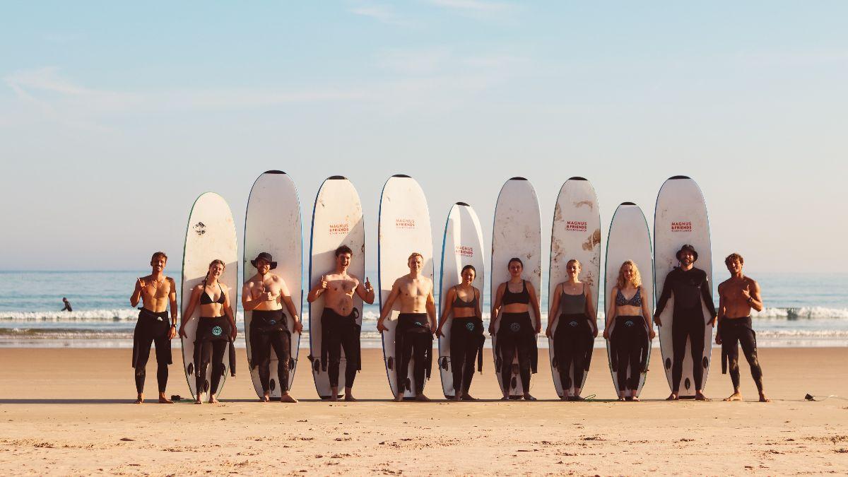 Surfgrupp som poserar på stranden i solen, framför deras surfbrädor