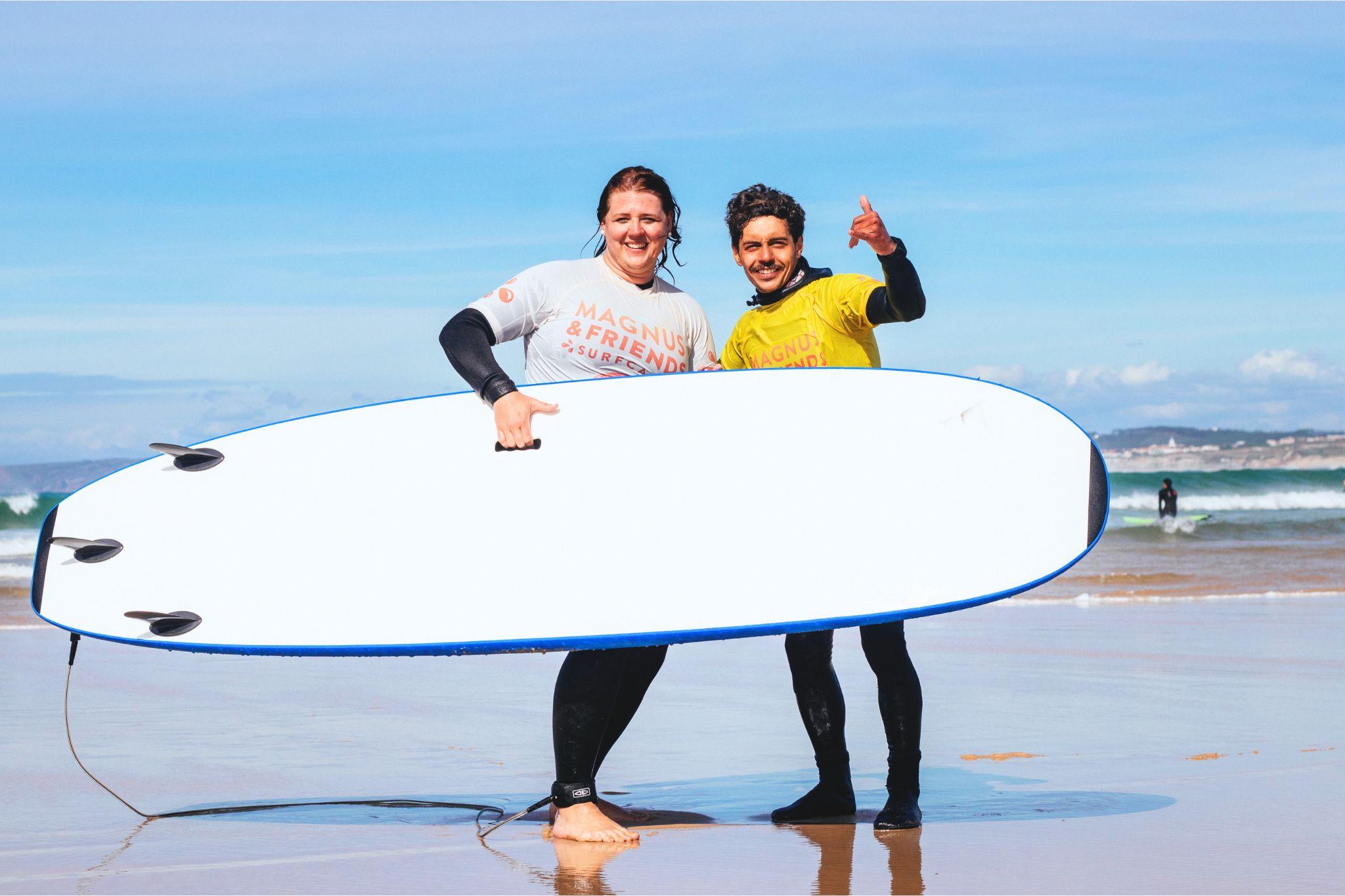 Två glada personer står på stranden med en surfbräda, njuter av en paus från coworking för en surflektion under en solig dag vid havet