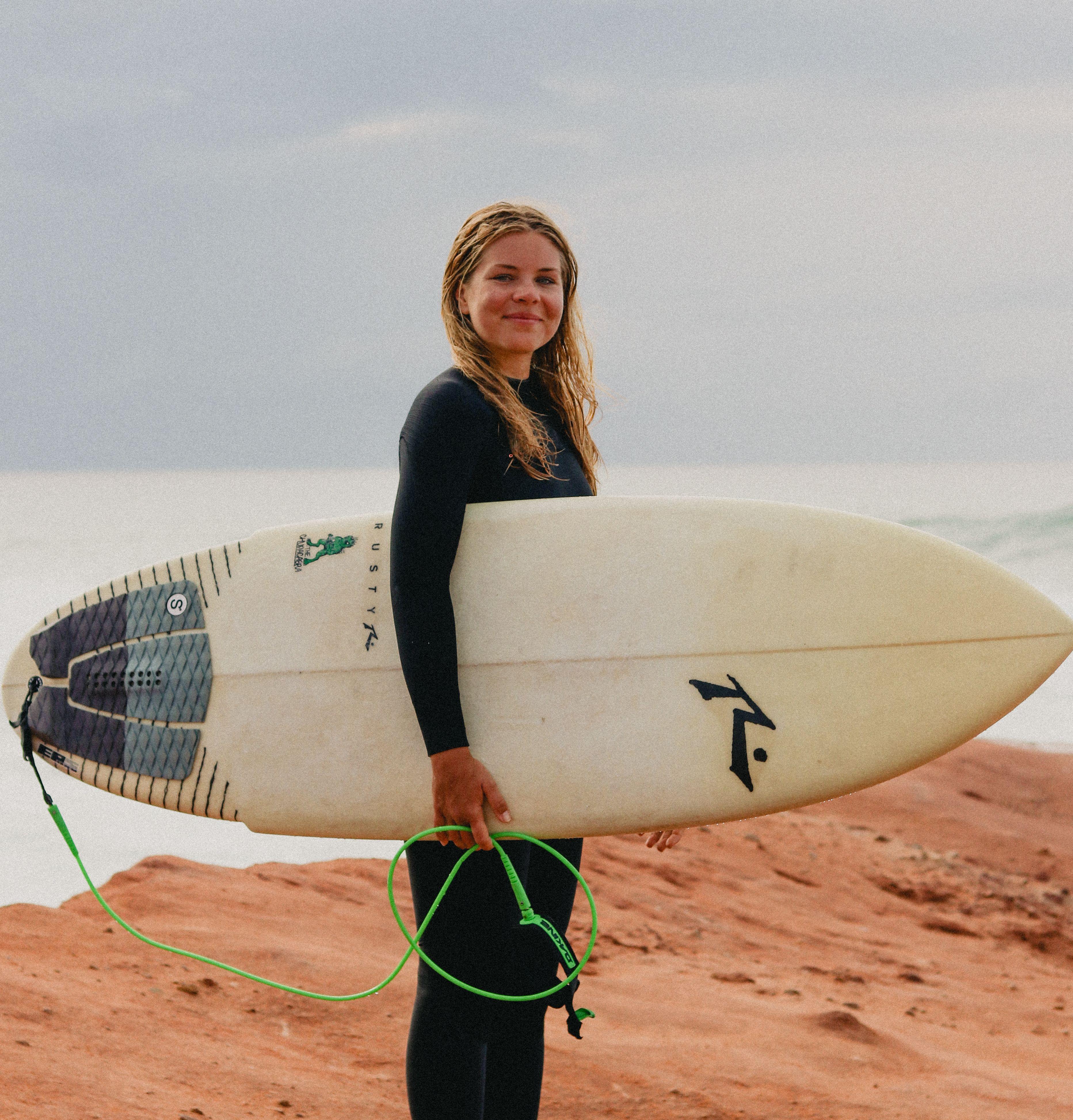 Elsa Bergh, camp manager på Magnus & friends med en surfbräda på klipporna