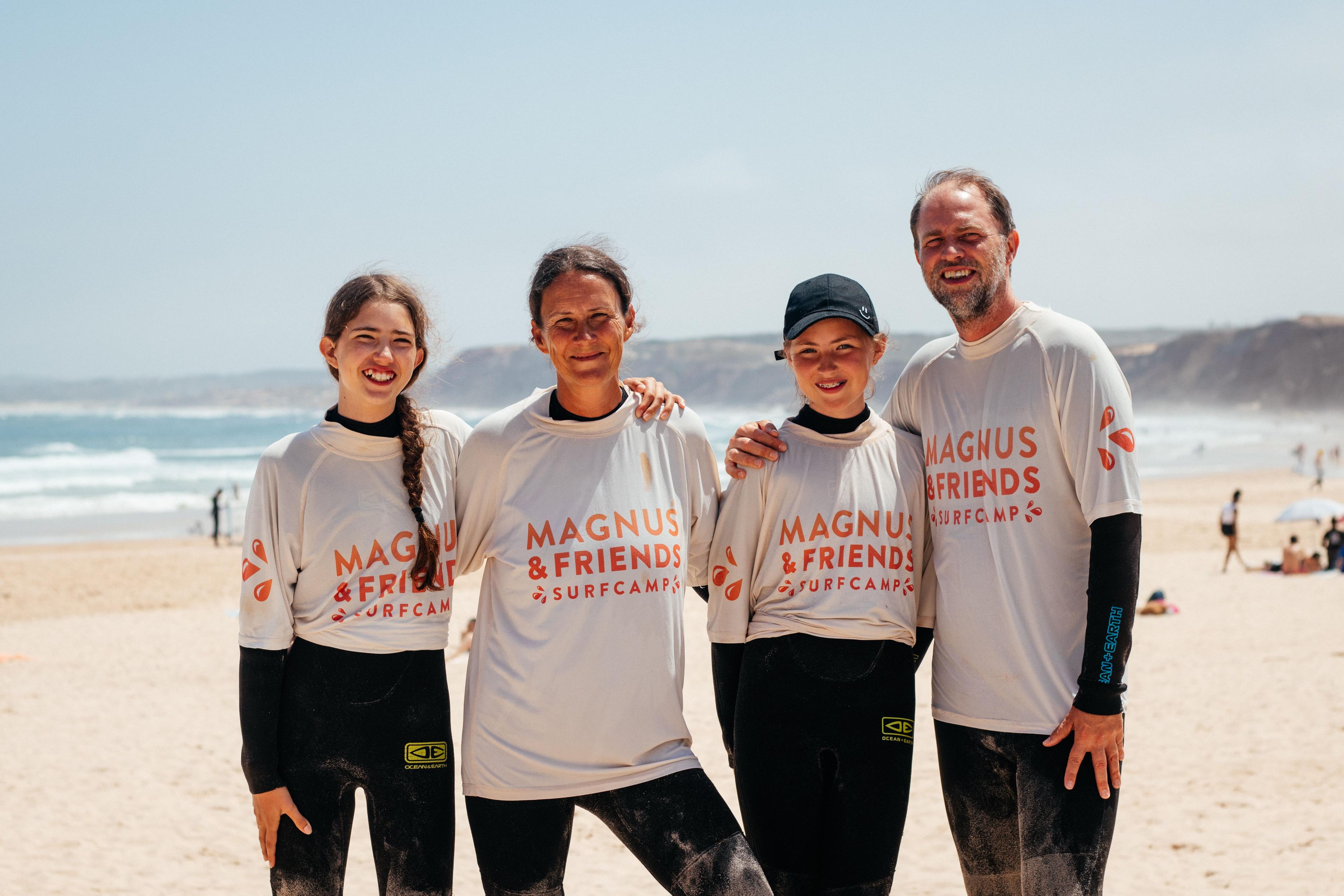 En glad familj i våtdräkter och Magnus & friends surftröjor tillsammans på stranden i Baleal efter en surflektion