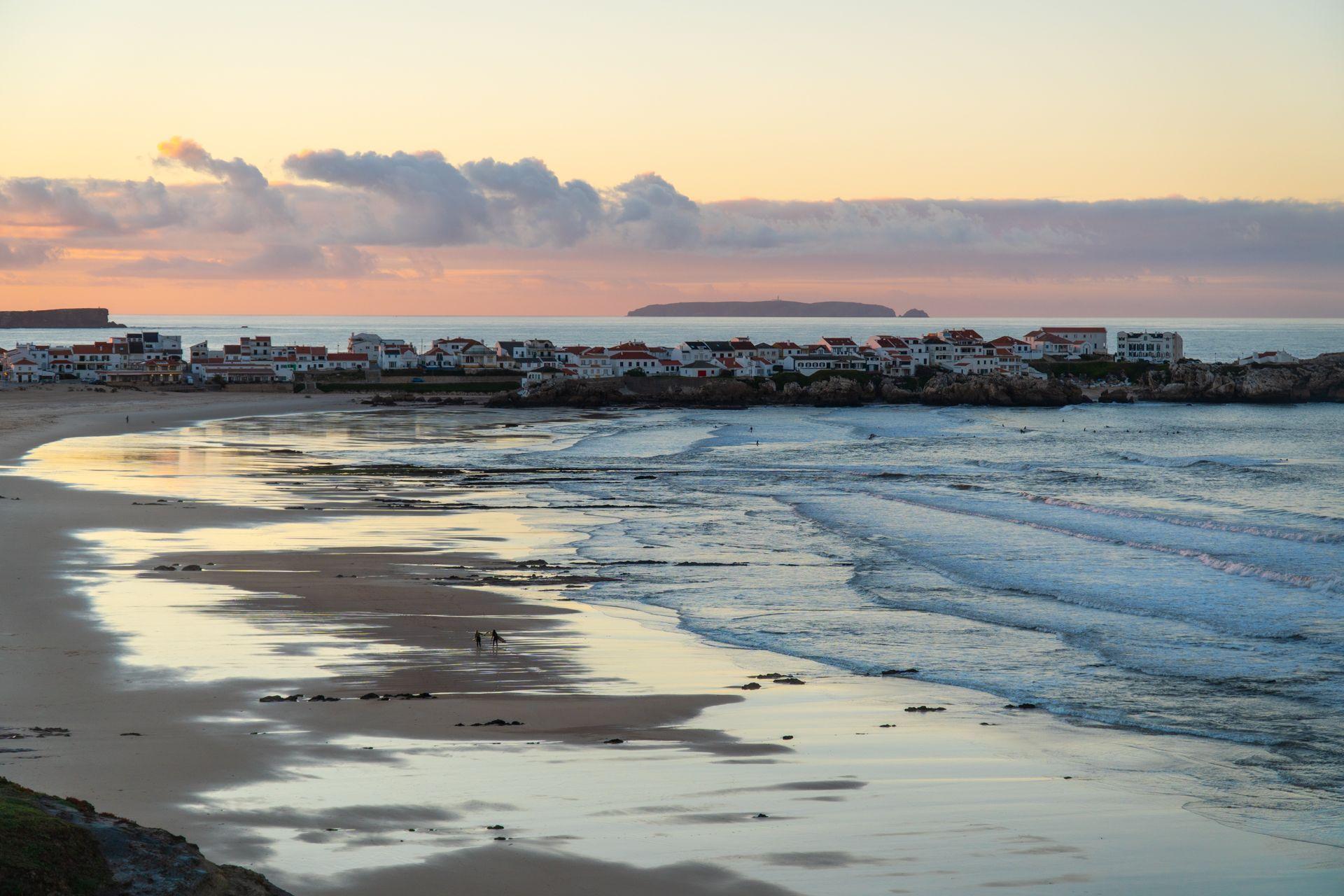 Vy över en  strand i solnedgång med små vågor som rullar in mot land