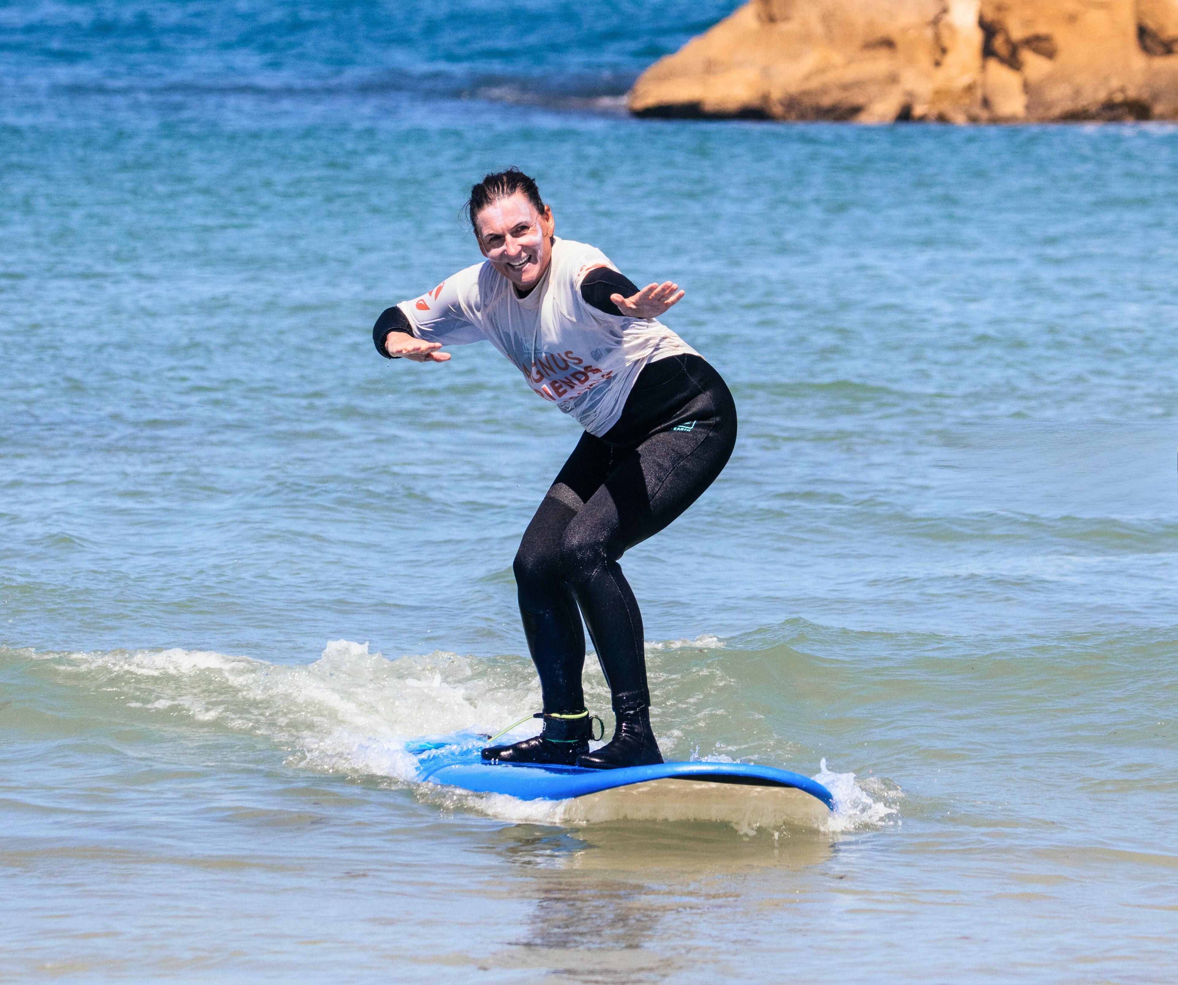 En glad surfare fångar en våg på en blå surfbräda, med klarblått hav och klippor i bakgrunden