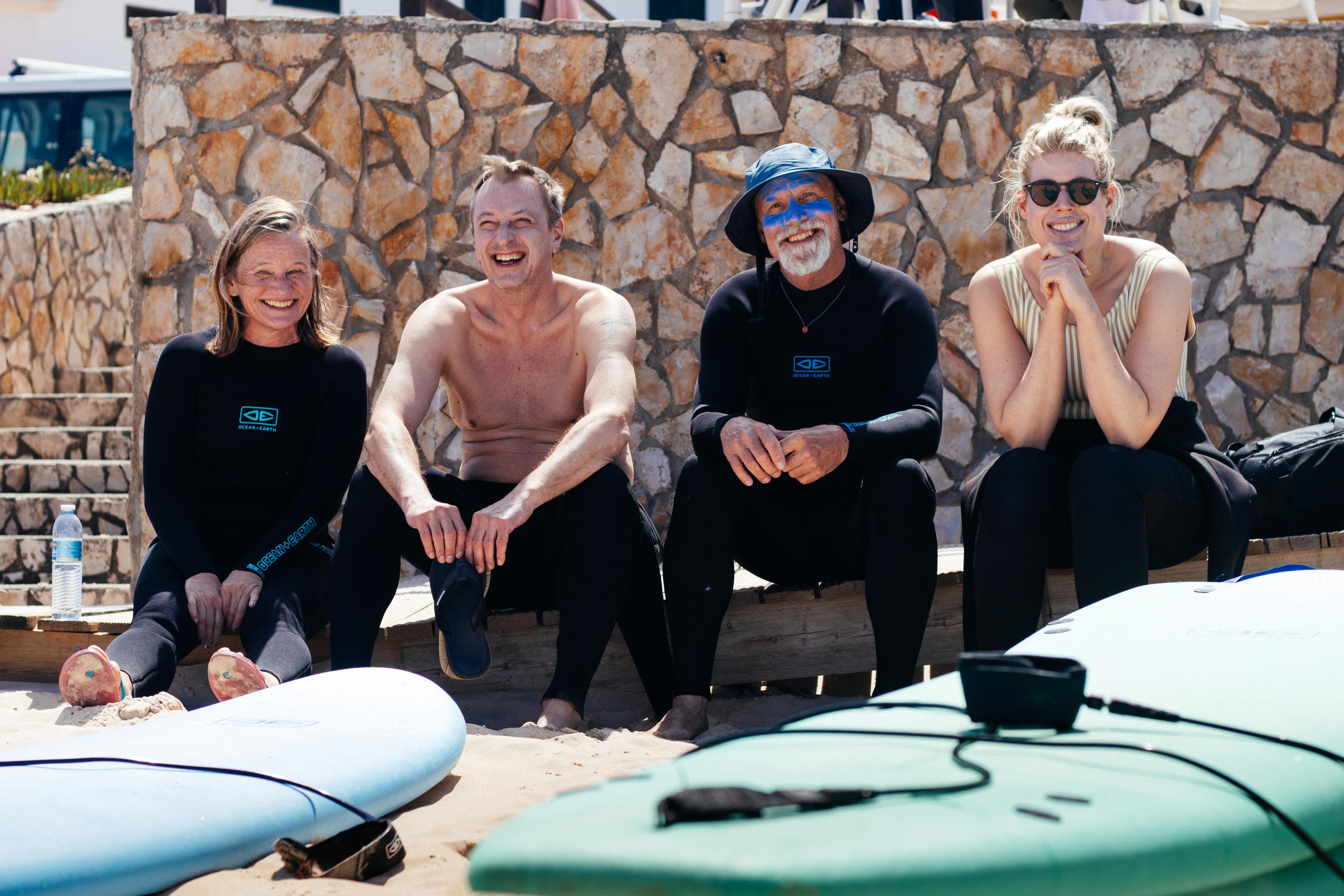 Fyra personer sitter avslappnat på stranden med surfbrädor i förgrunden, njuter av en paus under en inspirerande konferensresa vid havet