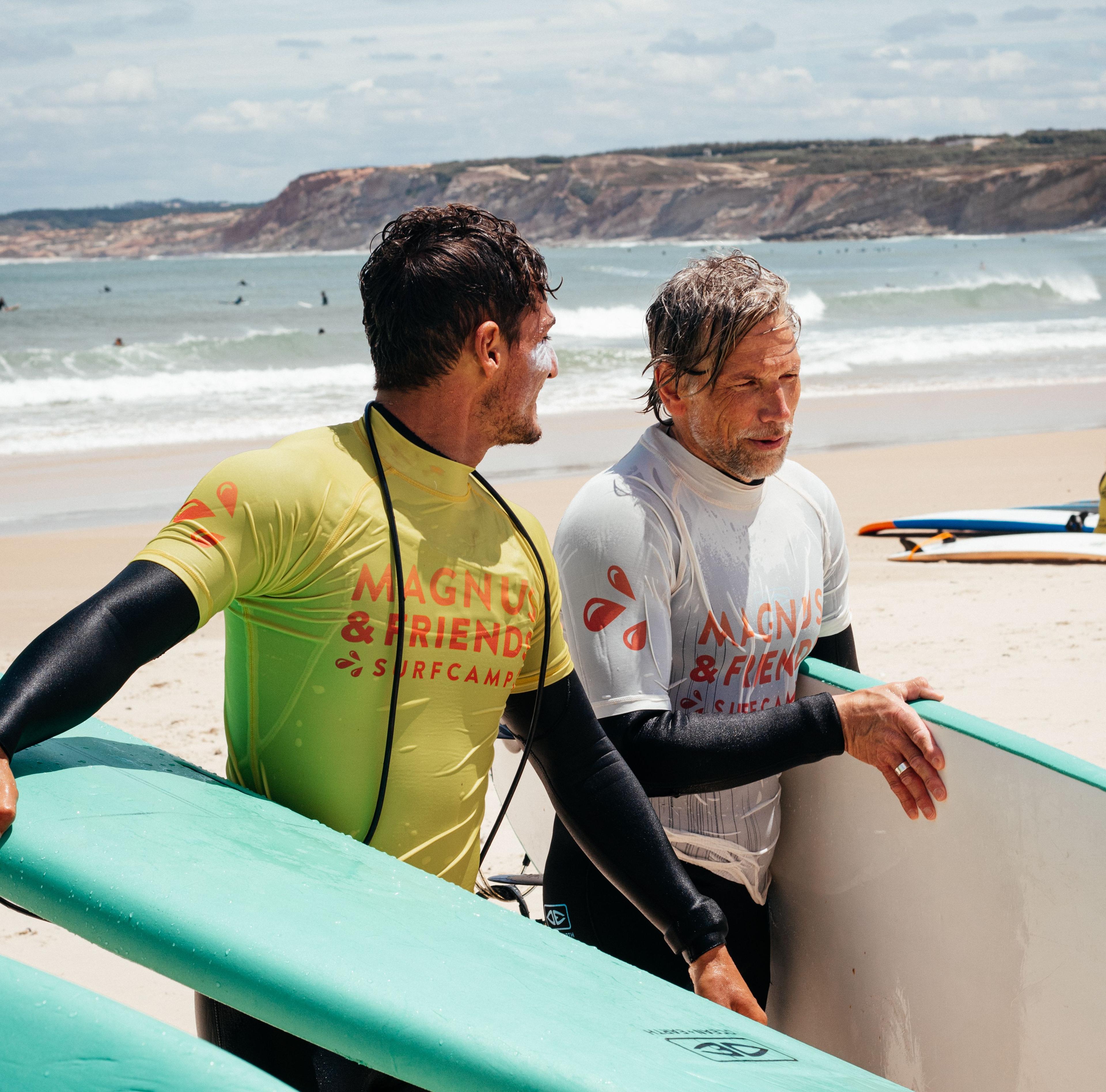 En deltagare och en surfinstruktör från Magnus & friends konferensresa pratar och håller i sina surfbrädor på stranden efter en lyckad surflektion