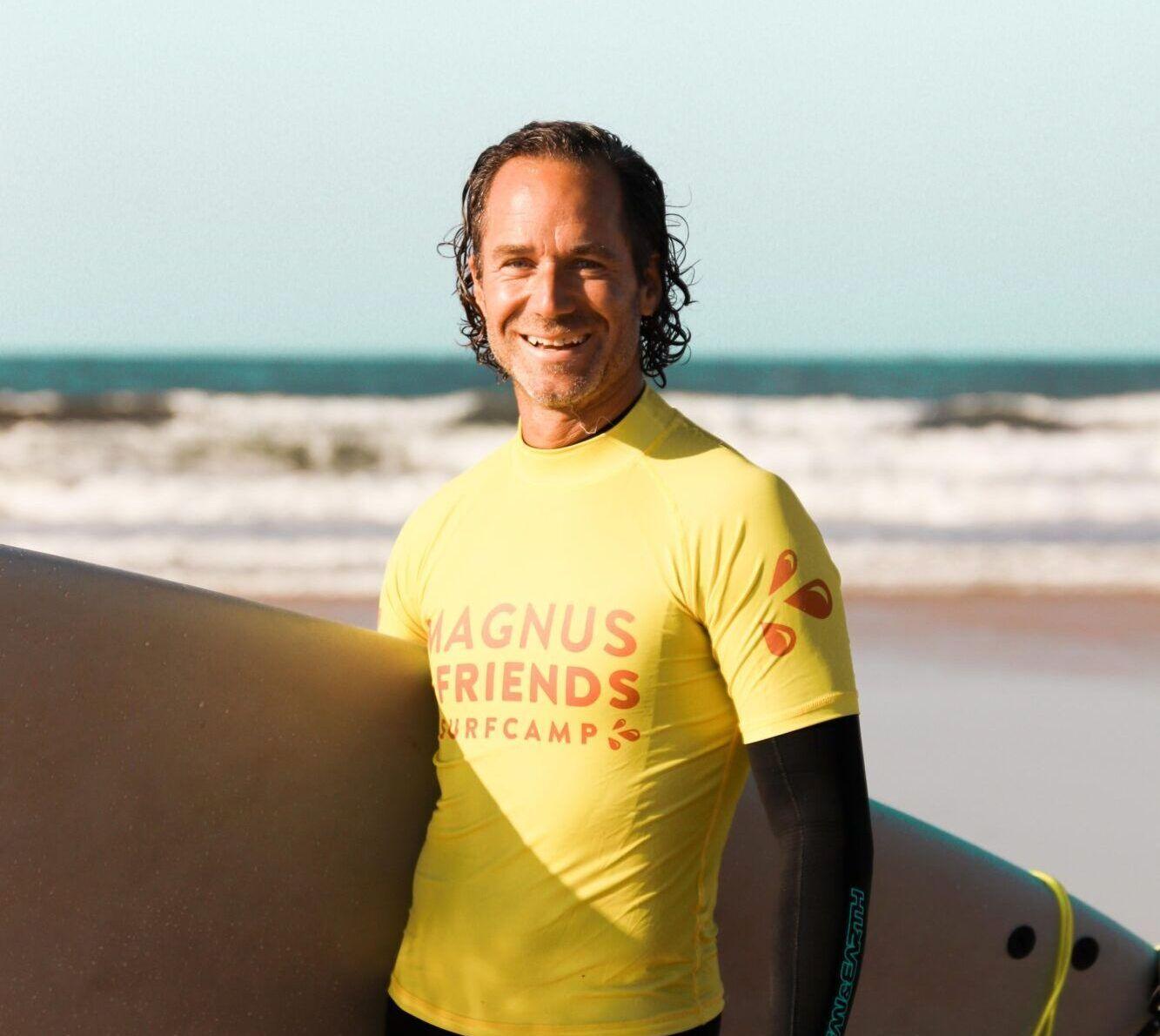 Magnus Haglund, grundare av Magnus & Friends Surfcamp, står med en surfbräda på stranden