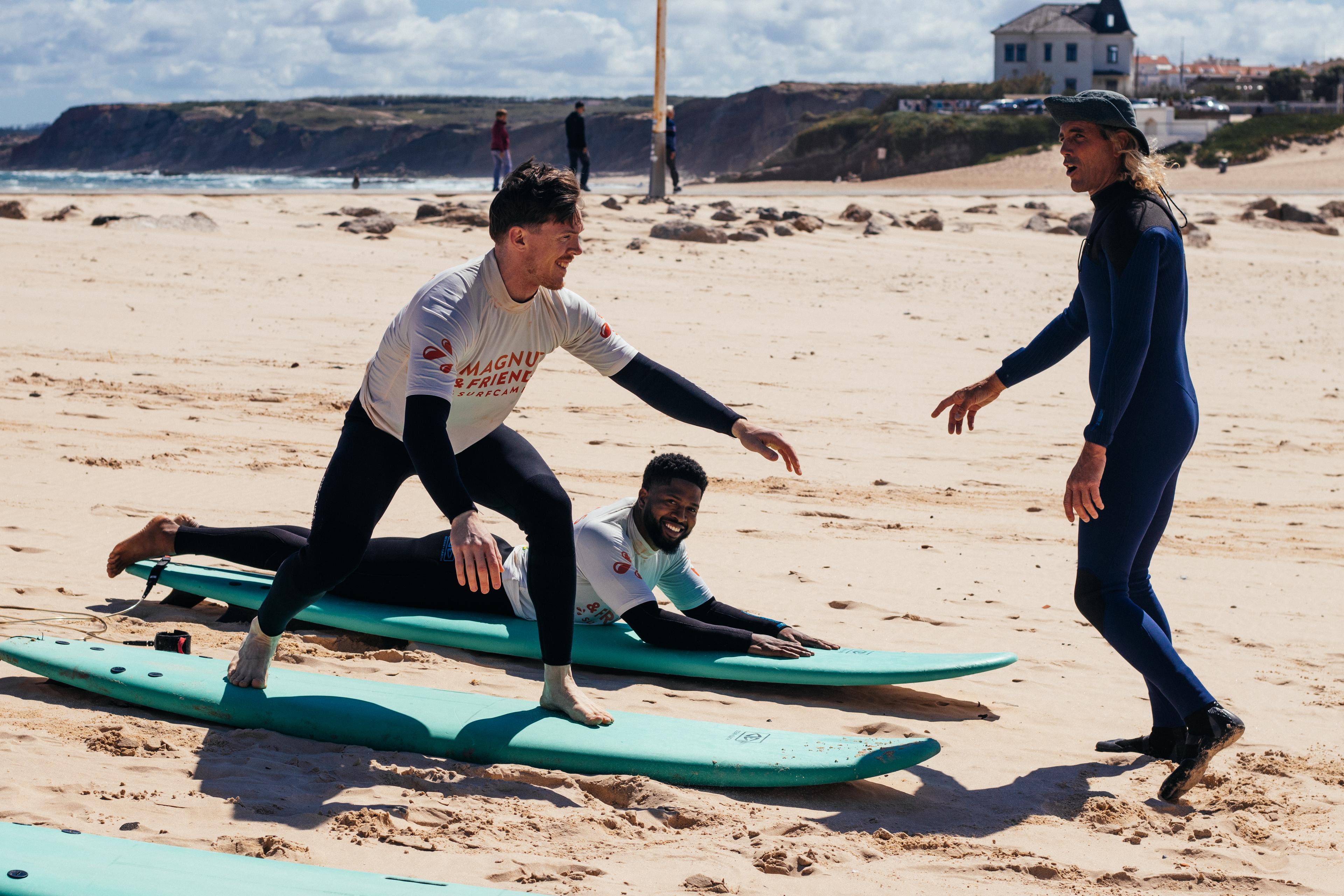 En surflektion på stranden där en instruktör guidar två deltagare som övar på pop-ups