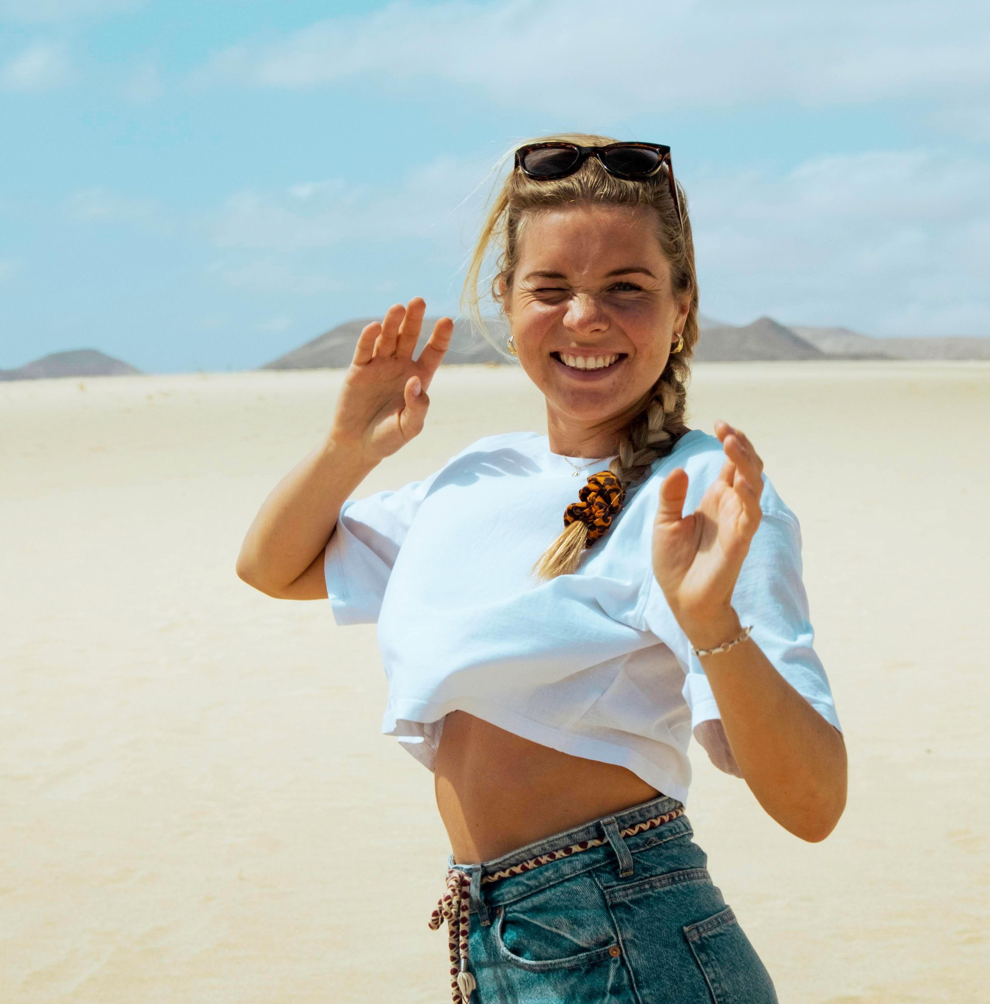 Elsa står i en solig ökenmiljö på Fuerteventura, omgiven av blå himmel och sanddyner