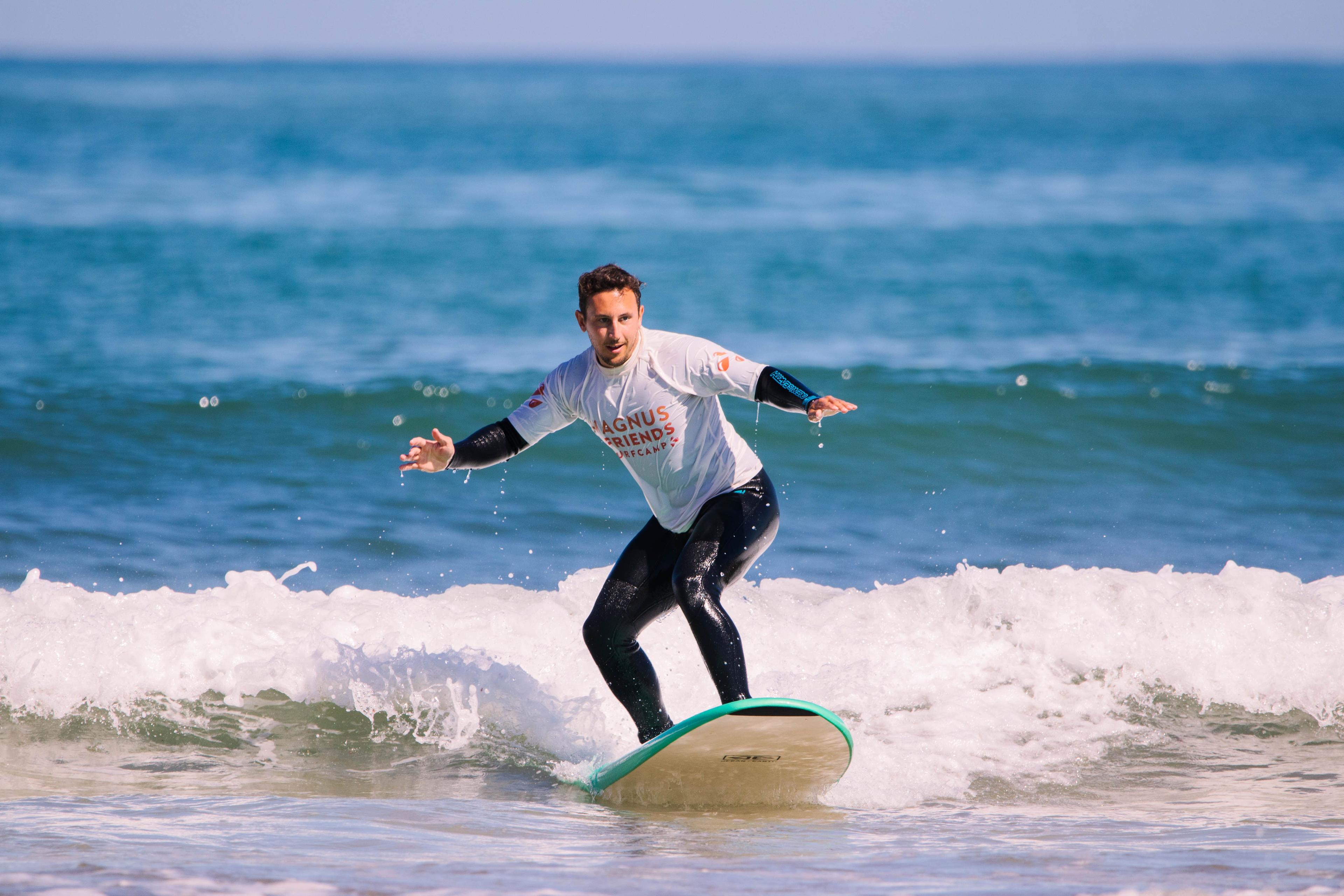 Surfare på en våg under en lektion med Magnus & friends surfcamp, omgiven av klarblått vatten