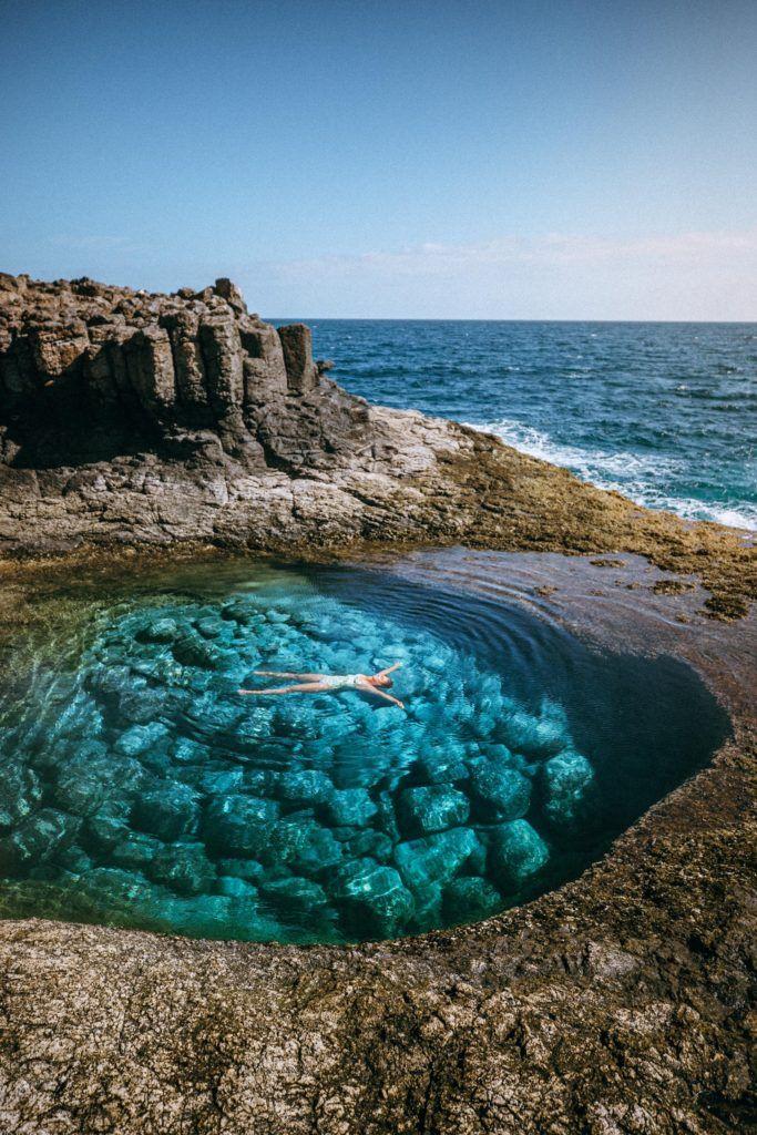 Person som badar i tide pools på Fuerteventura, med kristall klart blått vatten