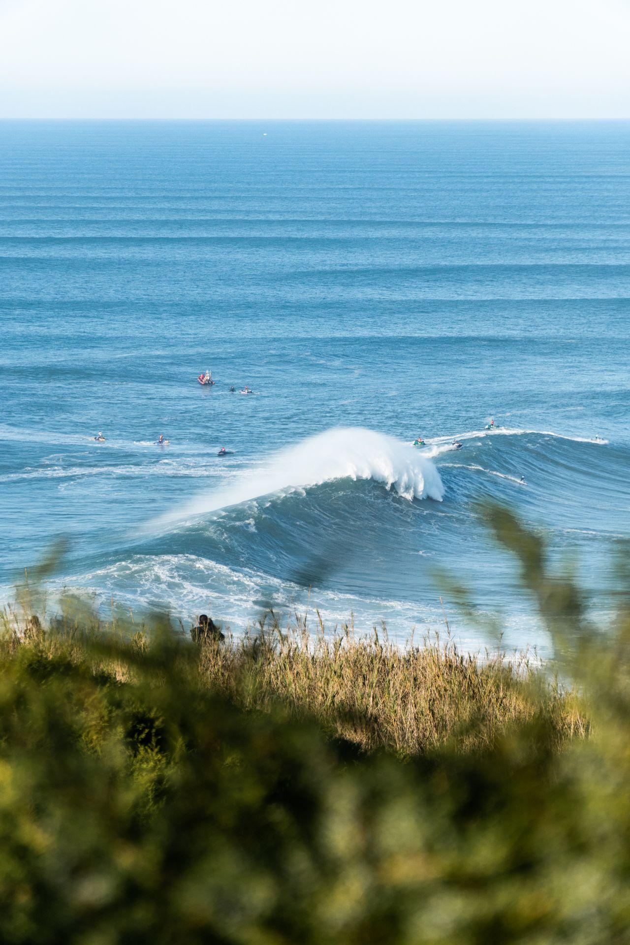 Stora vågor vid Nazaré med surfare och båtar i det blå havet