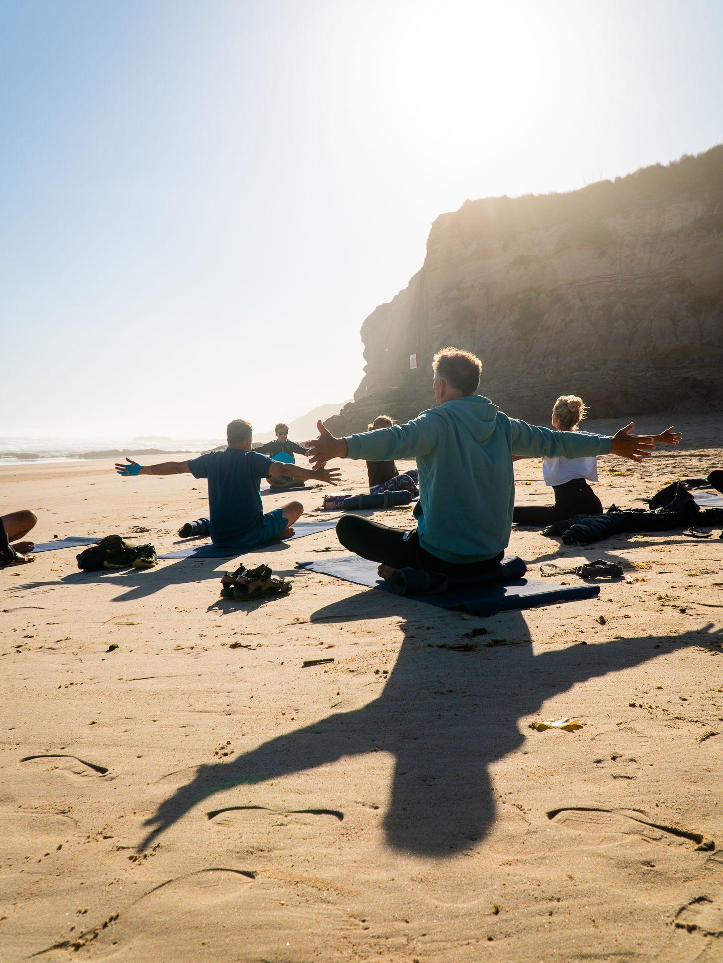 Yoga på stranden med klippor och solen i bakgrunden