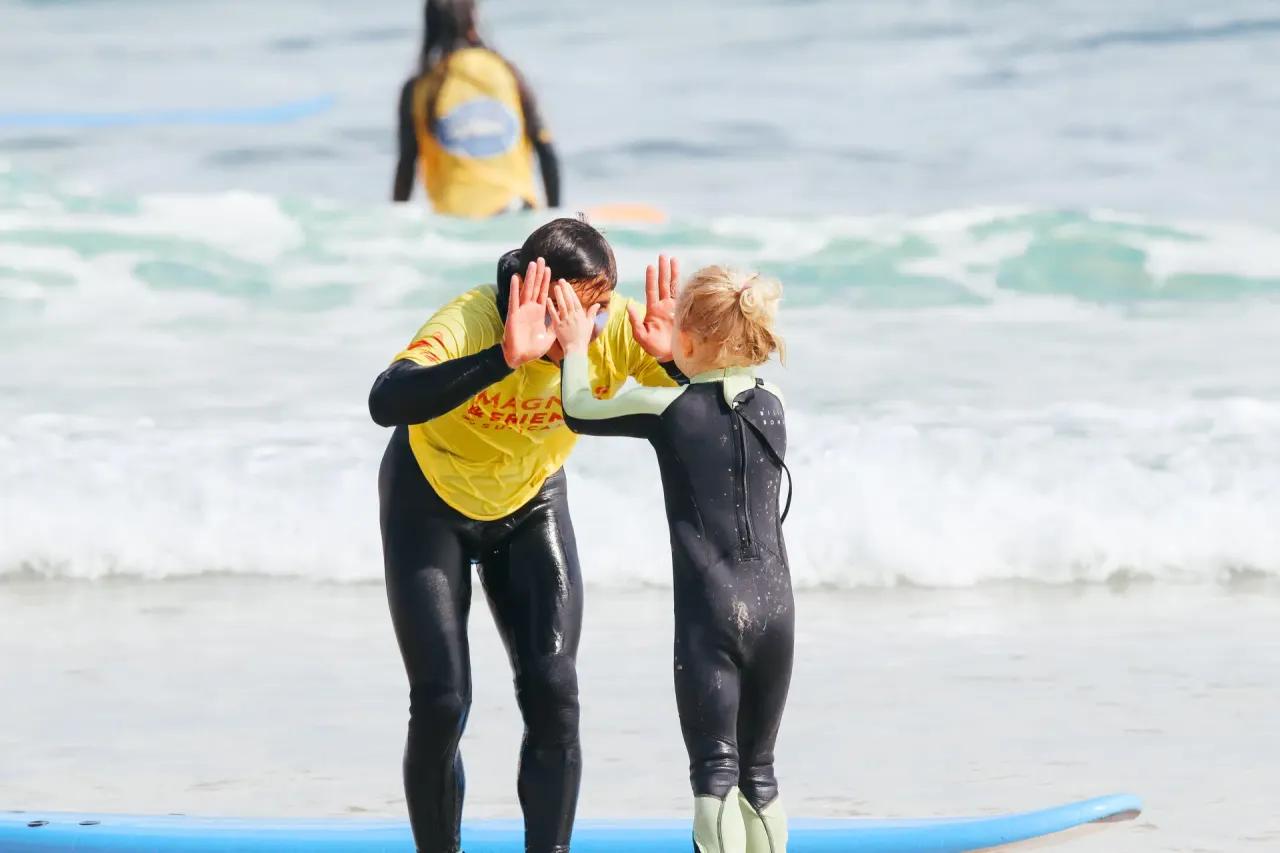 Surfinstruktör Dércio gör highfive med ett barn i vattnet efter hon har surfat en snygg våg