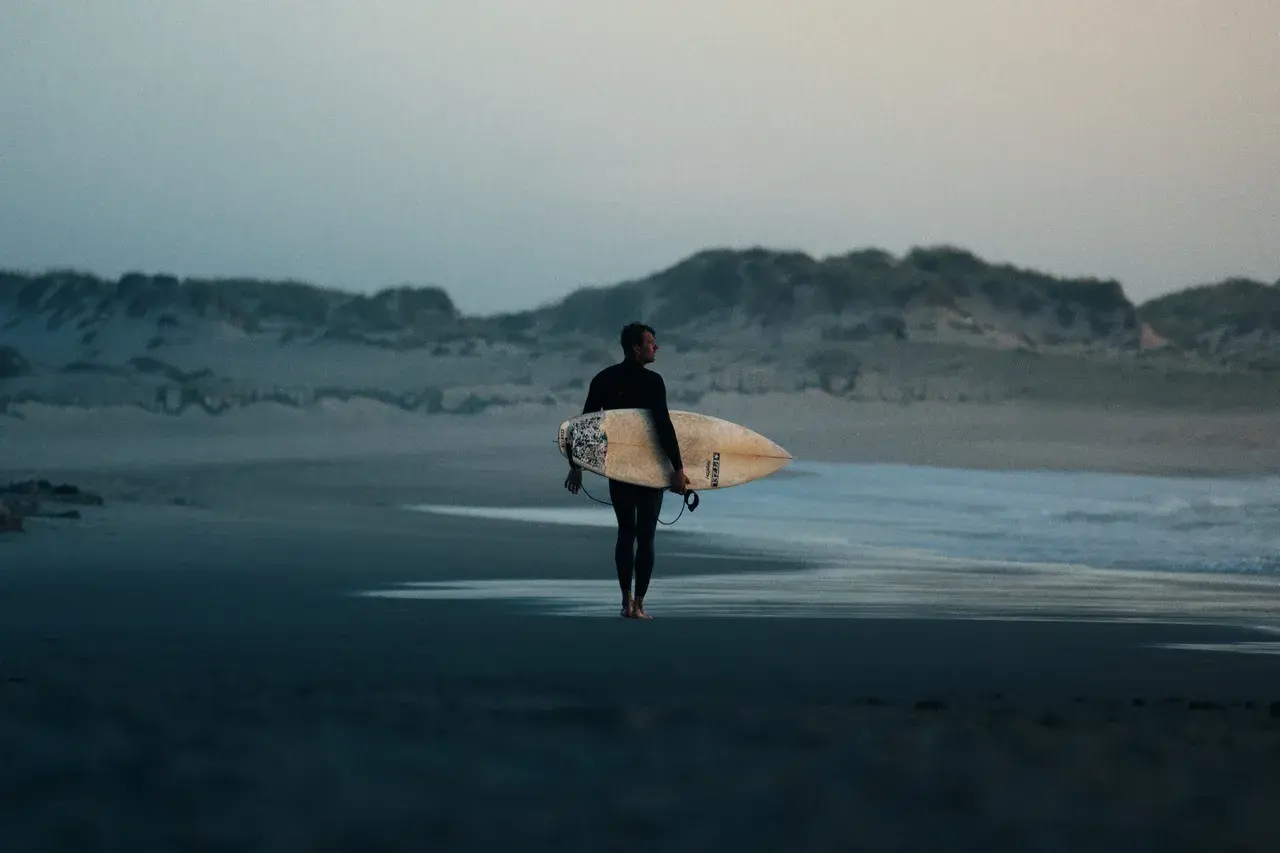 Person som går med surfbräda under armen, påväg mot havet