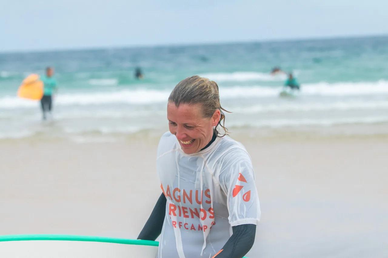 Henna går leende med surfbrädan på stranden